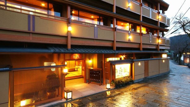 Uma ryokan japonesa tradicional com vários andares, fachada de madeira e iluminação acolhedora.
