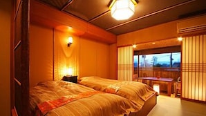 Um quarto tradicional japonês, com uma cama grande, uma mesinha e uma porta de correr para uma varanda.