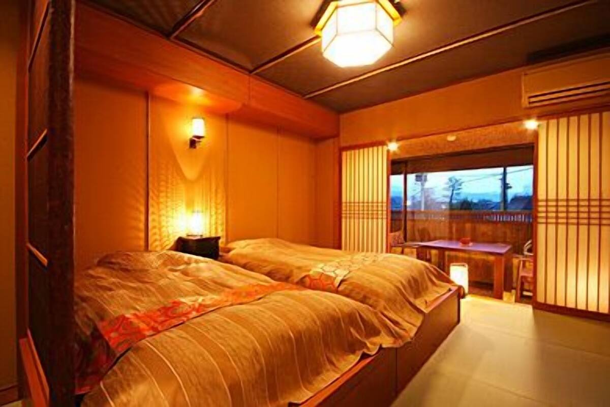 Une chambre de style japonais traditionnel, avec un grand lit, une petite table et une porte coulissante donnant sur un balcon.