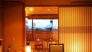Um quarto japonês tradicional com tatames, uma mesa baixa com assento, uma cadeira e um painel deslizante shoji.