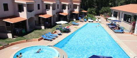 Una piscina al aire libre, sombrillas, sillones reclinables de piscina