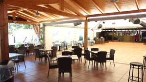 Un café en plein air avec des tables et des chaises en bois, un sol carrelé et un espace couvert sur lequel est affiché un panneau indiquant « CUBASI ».