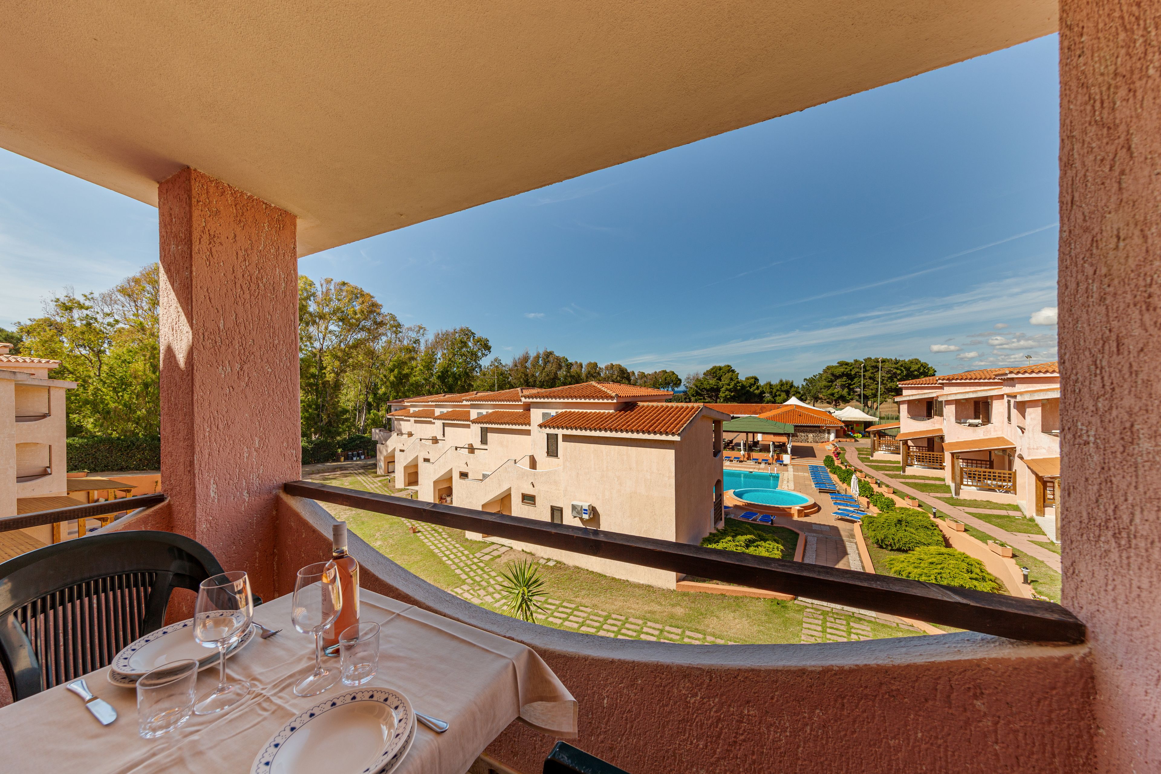 Un balcon avec une table dressée pour le dîner, donnant sur une piscine et sur des bâtiments aux toits recouverts de tuiles rouges.