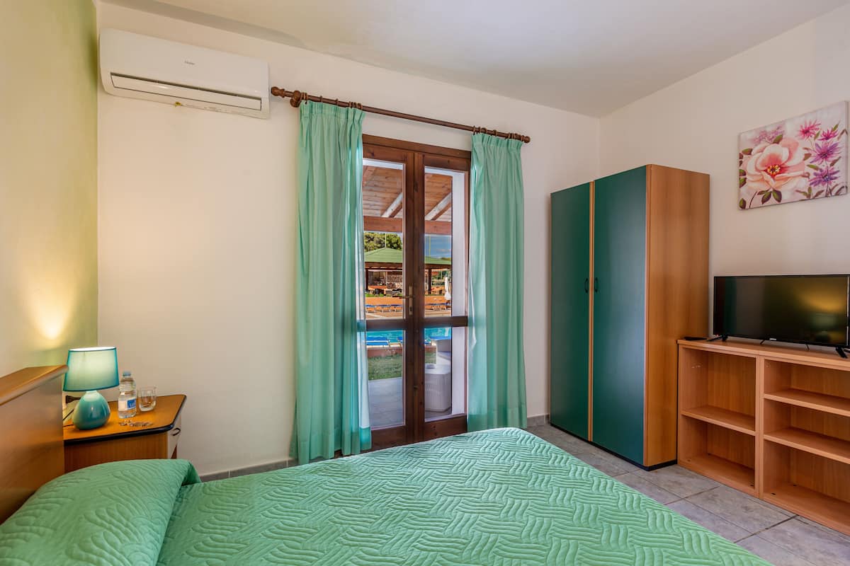 Un dormitorio con cama, televisor, armario y ventana con cortinas.