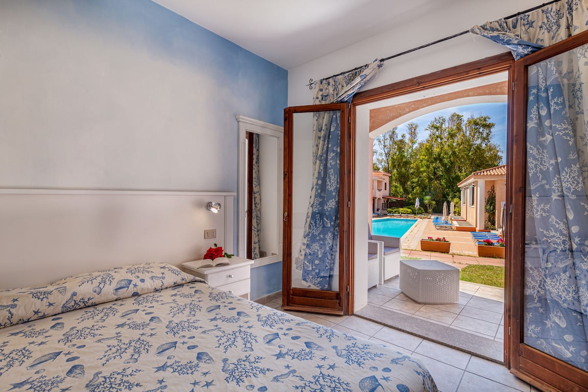 Un dormitorio con cama, mesita de noche, espejo y vistas a un área de piscina al aire libre.