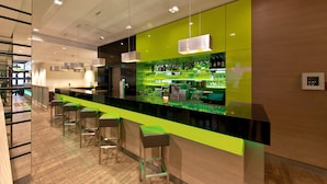 Un espace bar moderne avec un comptoir vert, de nombreux tabourets et un espace bien éclairé grâce à un éclairage installé au plafond.