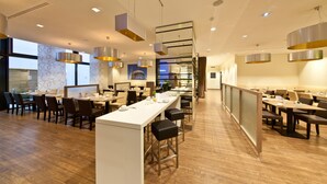 A modern restaurant with a long counter, multiple seating areas, and contemporary lighting fixtures. - Garner Hotel Berlin - Charlottenburg by IHG (Berlin)
