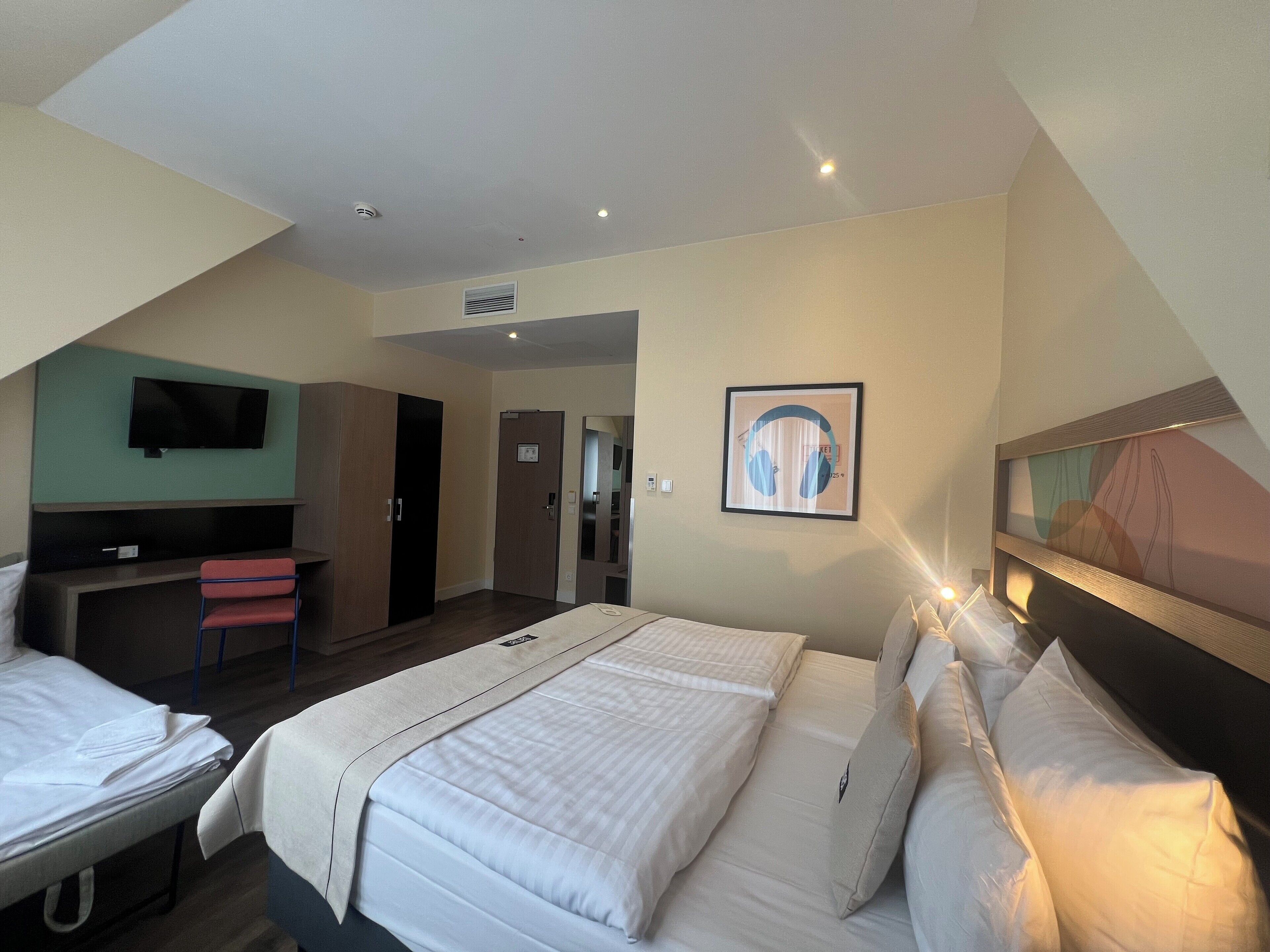A hotel room with a bed, a desk, a chair, a television, and a framed artwork on the wall.