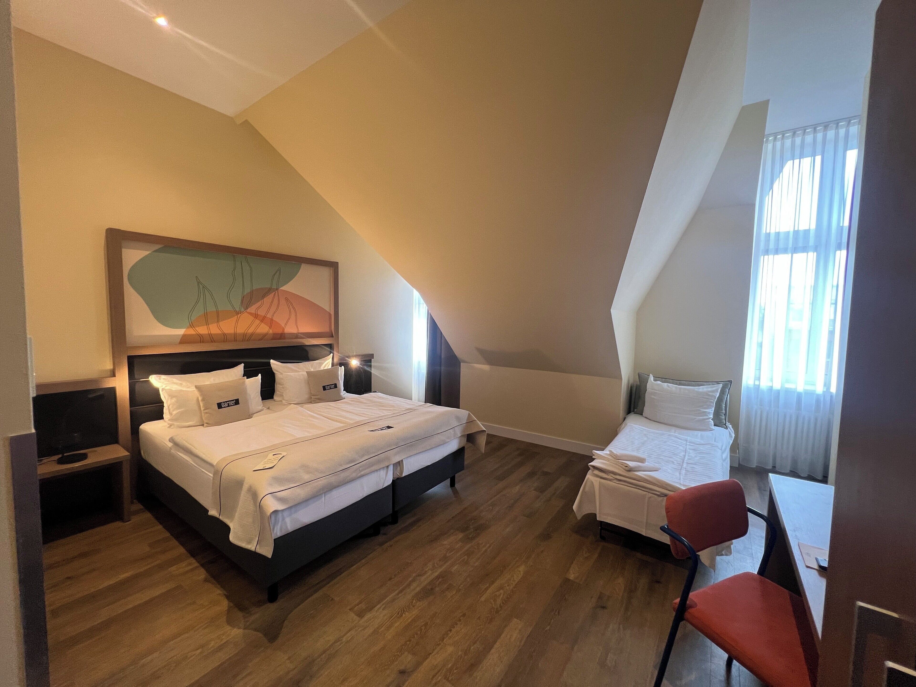 Una habitación de hotel con una cama grande, una cama más pequeña, un escritorio y una silla.