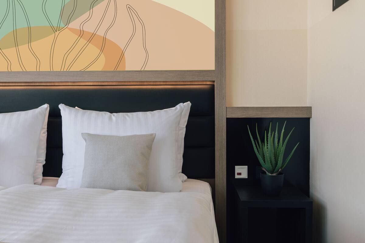 A neatly made bed with white and grey pillows, a dark headboard, and a wall art piece above it.