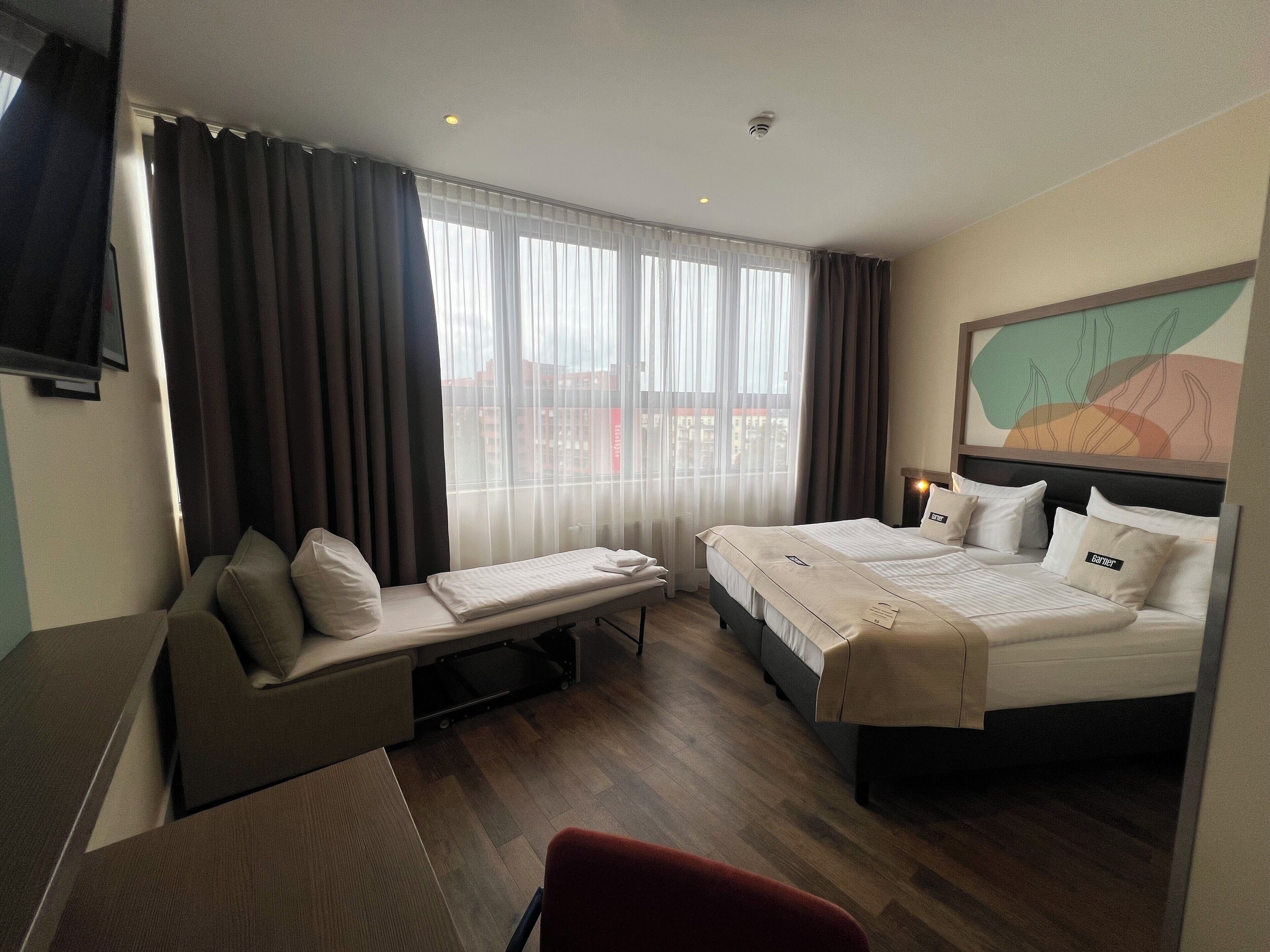 Een hotelkamer met een bed, een bureau, een stoel en een raam met gordijnen.