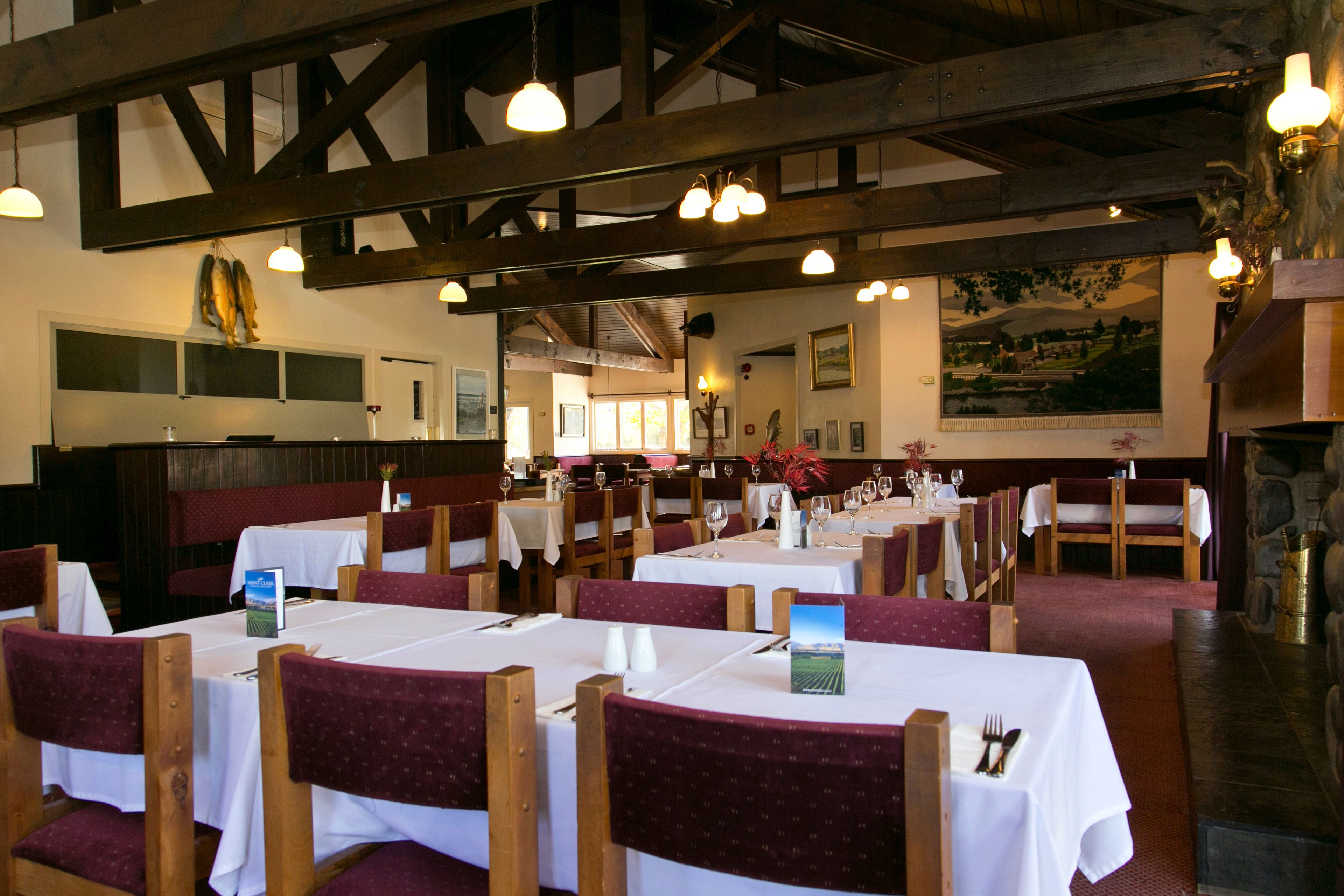 A restaurant with multiple tables set for dining, wooden beams on the ceiling, and a stone wall.