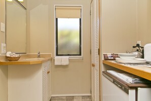 A bathroom with a sink, a window, a towel rack, a basket, and a dish rack.