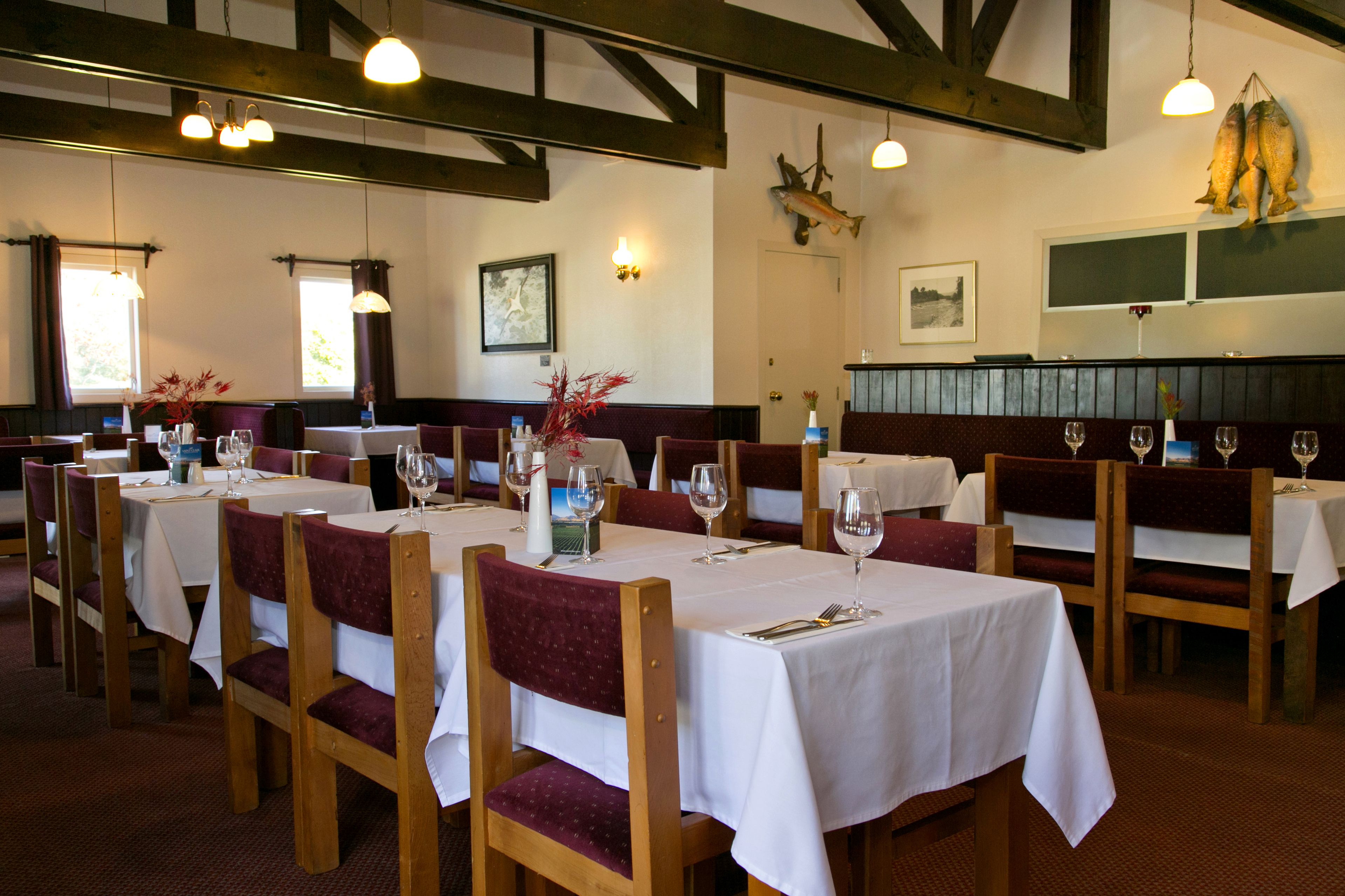 A restaurant with wooden tables and chairs, white tablecloths, and red cushioned seats.