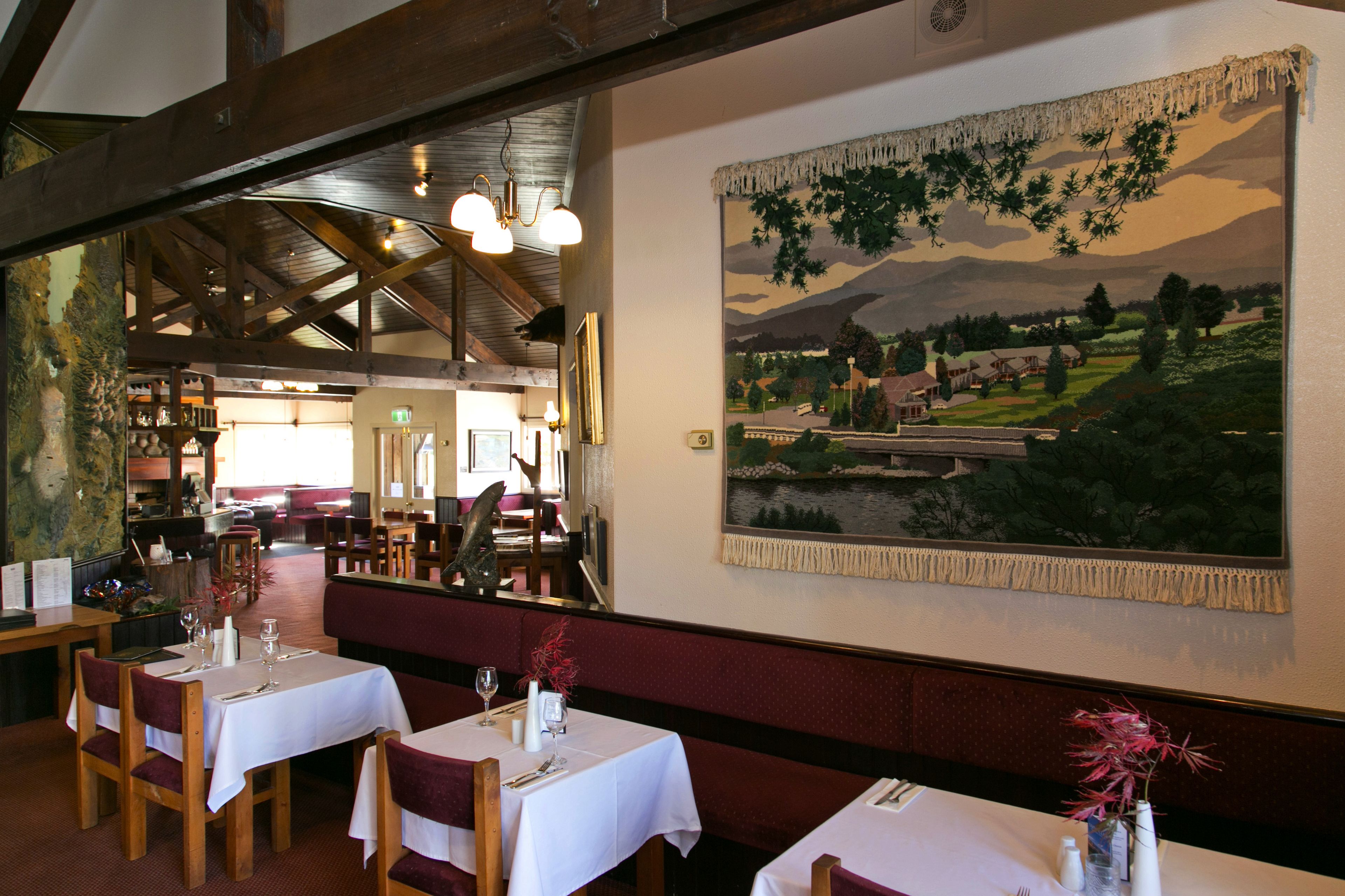 A restaurant with wooden tables and benches, a large painting on the wall, and a high ceiling with exposed beams.