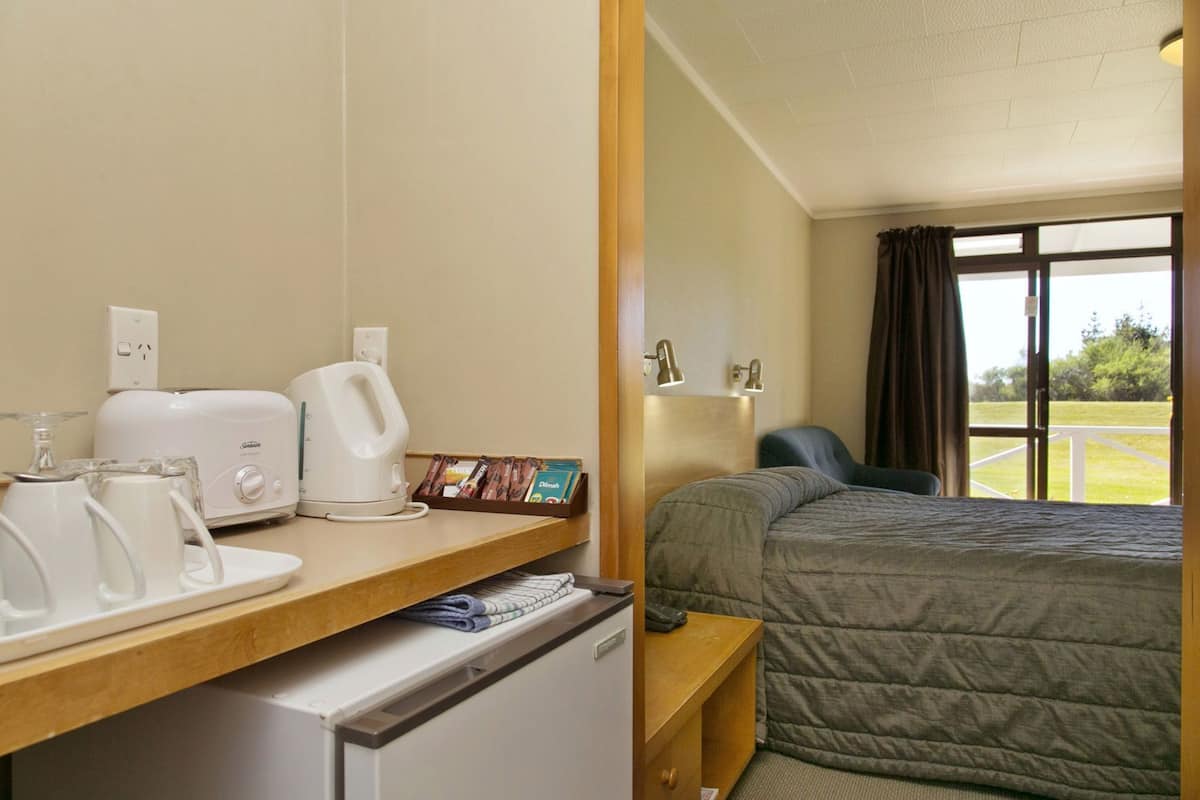 A hotel room with a bed, a desk with a toaster, a kettle, and a coffee maker. There is a window with curtains and a view of the outdoors.