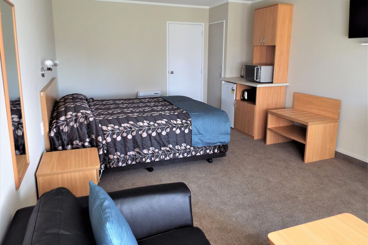 A compact room with a bed, a desk, a chair, a microwave, and a small refrigerator.