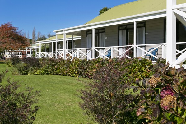A row of white cabins with balconies, surrounded by well-maintained gardens and a clear blue sky.