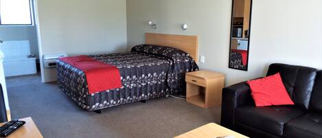 A hotel room with a bed, a bedside table, a black leather sofa, a wooden coffee table, and a mirror on the wall.