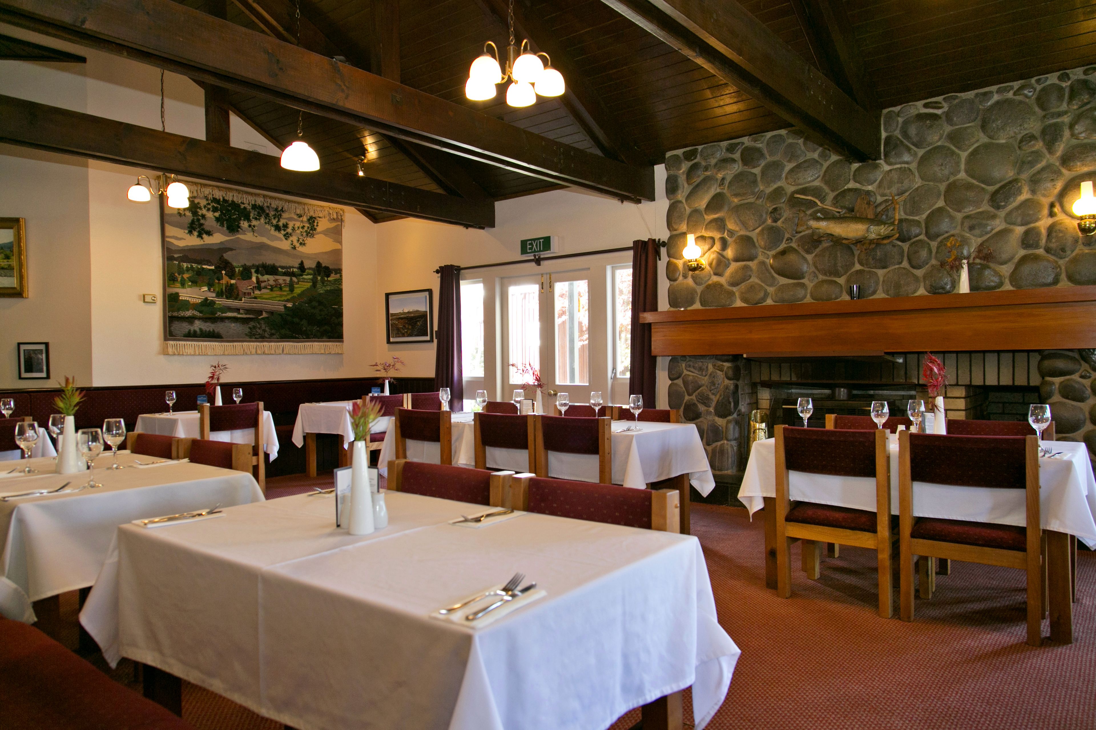 Un restaurante con varias mesas, sillas de madera y una pared de piedra.