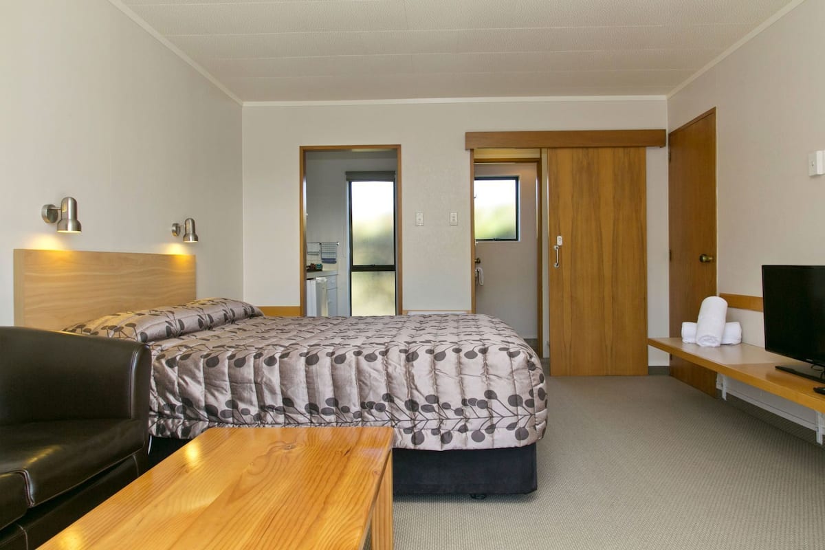 A hotel room with a bed, a desk, a TV, a chair, and a door.