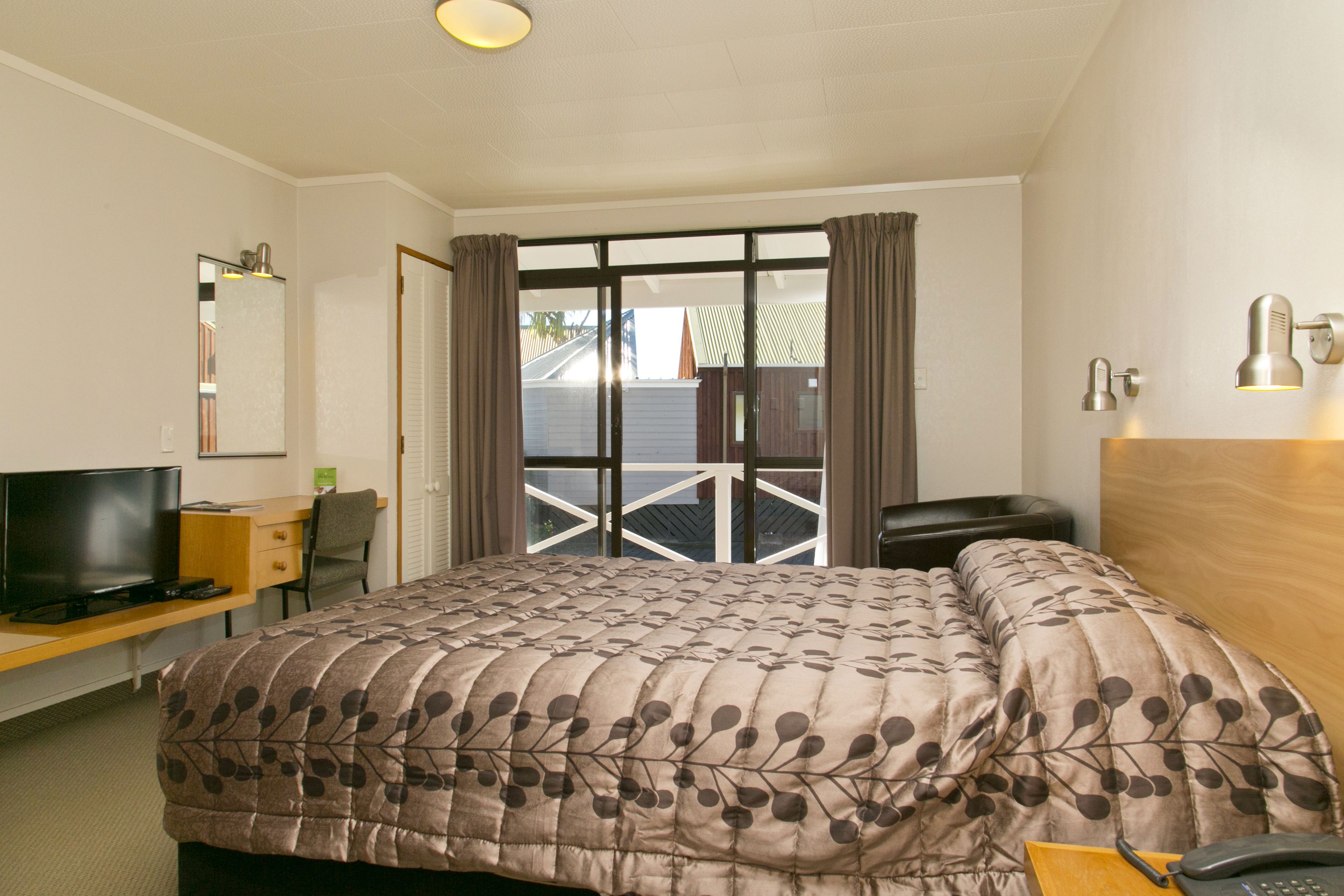 A hotel room with a bed, a desk with a computer, a TV, a chair, a phone, and a window with curtains.