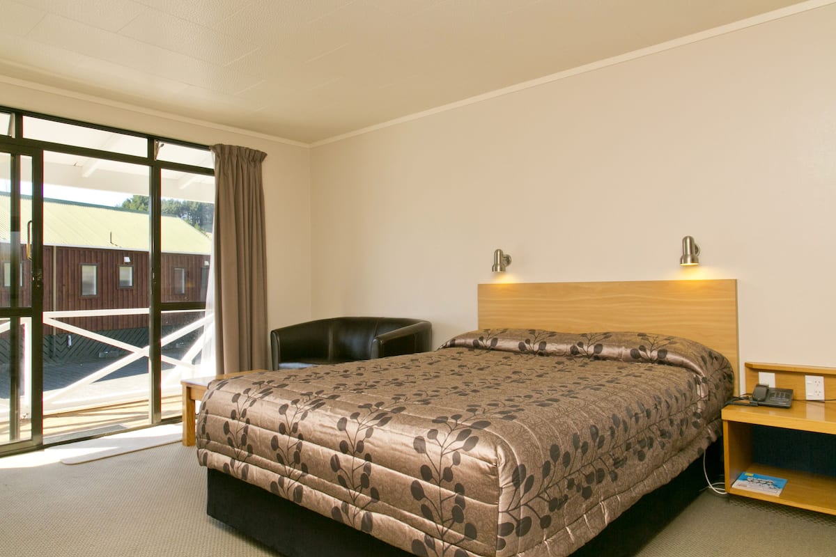 A hotel room with a large bed, a desk, and a chair. There is a window with a view of a building outside.