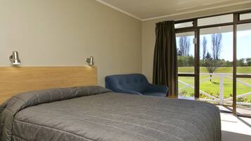 Habitación de hotel con una cama grande, una silla azul y vistas a un paisaje verde a través de un ventanal.