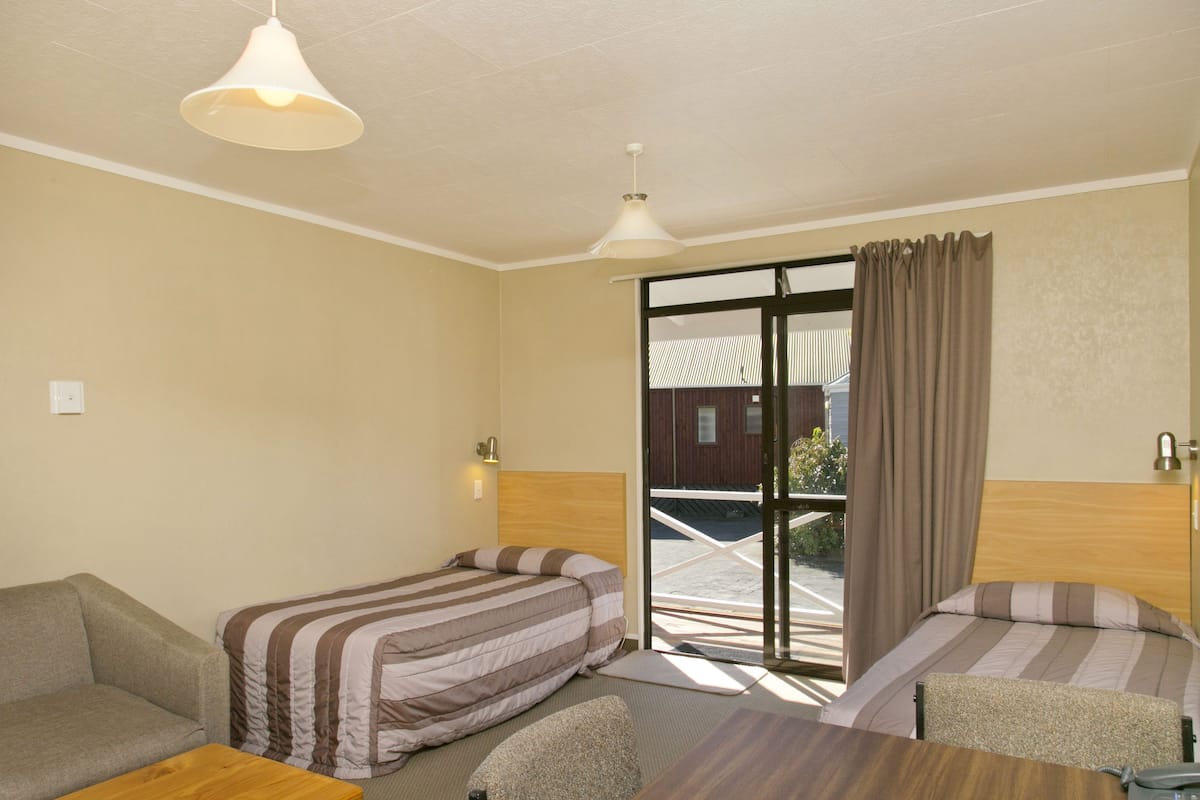 A hotel room with two beds, a sofa, a wooden table, and a view of the outside.