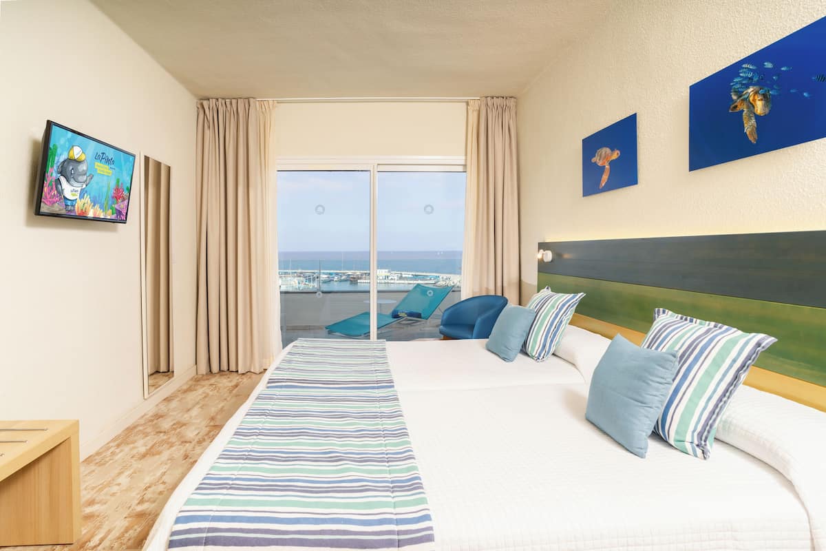 Ett hotellrum med en stor säng, utsikt över havet, en TV och konstverk på väggarna.