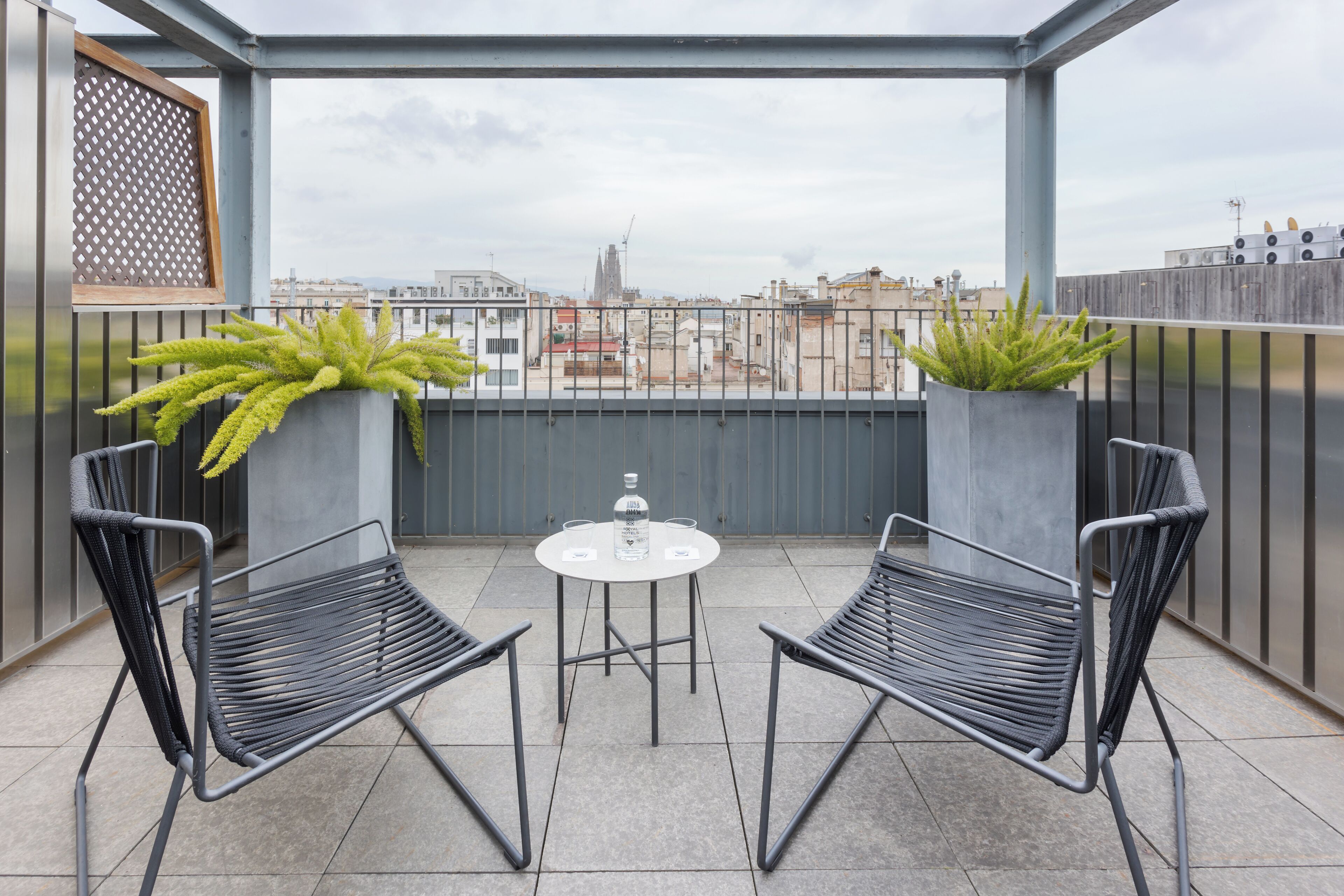 Un balcon avec deux chaises en métal noir et une petite table ronde, chacune agrémentée d’un pot de fleurs.