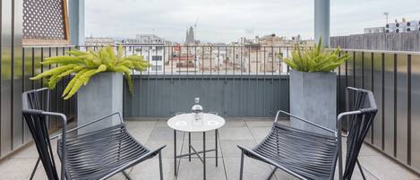 Un balcon avec deux chaises en métal noir et une petite table ronde, chacune agrémentée d’un pot de fleurs.