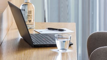 Una computadora portátil sobre una mesa de madera con una botella de whisky Royal Hotel Barcelona, un vaso de agua y un bolígrafo.