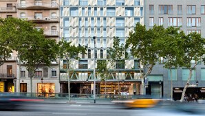 Un hotel moderno con fachada de vidrio, varios balcones y una planta baja con locales comerciales.