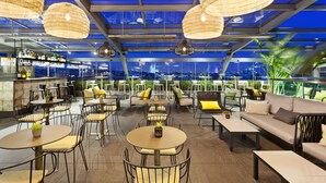 Un bar en la azotea con mesas y sillas, una zona de bar y vistas de la ciudad.