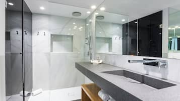 A modern bathroom with a large mirror, two sinks, and a shower area.