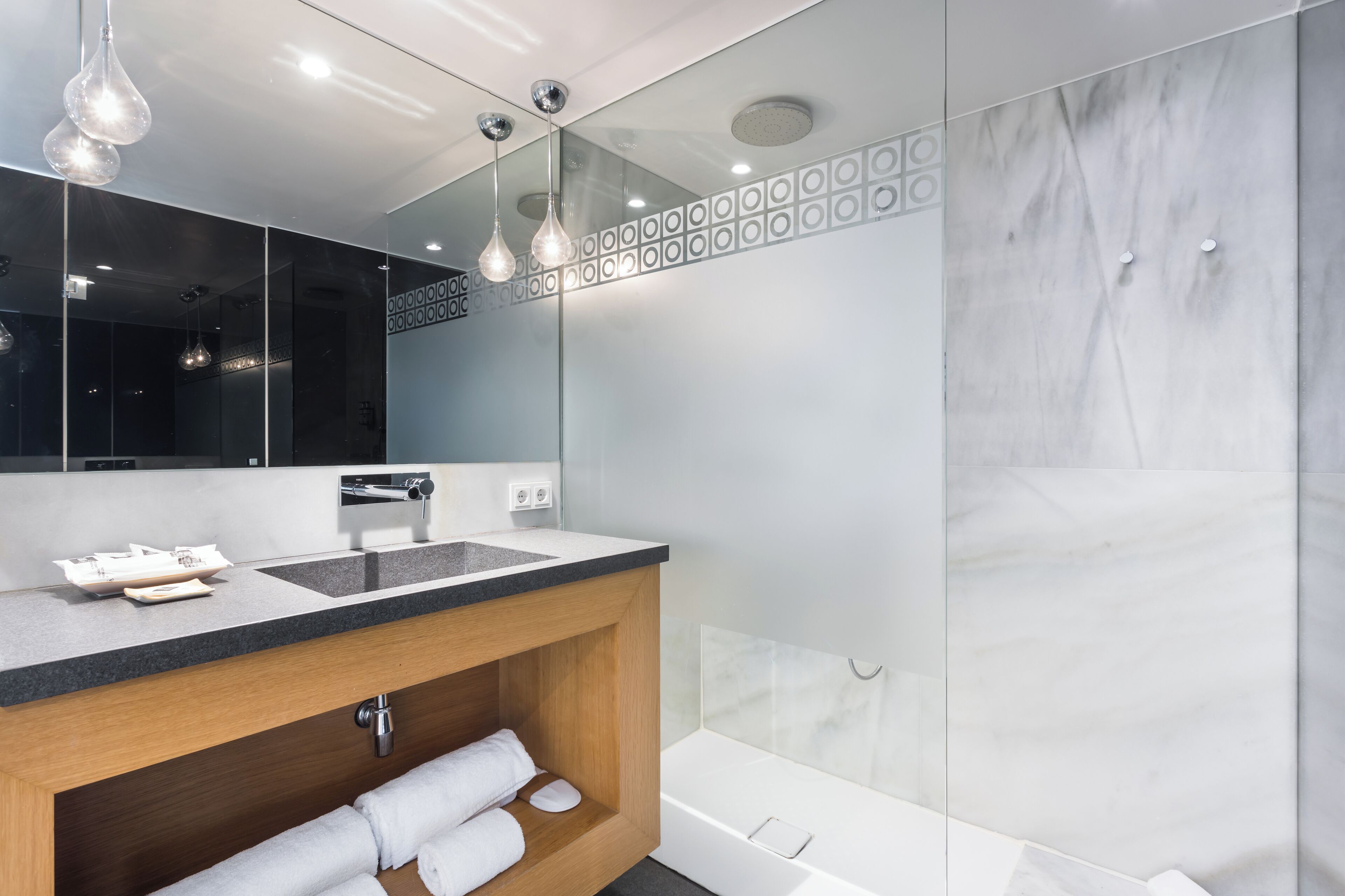Un baño moderno con un espejo grande, un tocador de madera, una bañera blanca y un box de ducha de cristal.