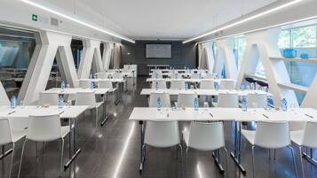Un salón de conferencias con mesas y sillas blancas, botellas de agua y una pantalla mostrando "R YAL HOTELS".