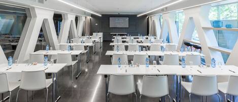 A conference room with white tables and chairs, water bottles, and a screen displaying "R YAL HOTELS".