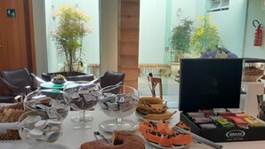 A buffet table with various desserts and snacks, including a chocolate cake, mango slices, and a selection of packaged goods. - Garibaldi Business Hotel (Porto Alegre)
