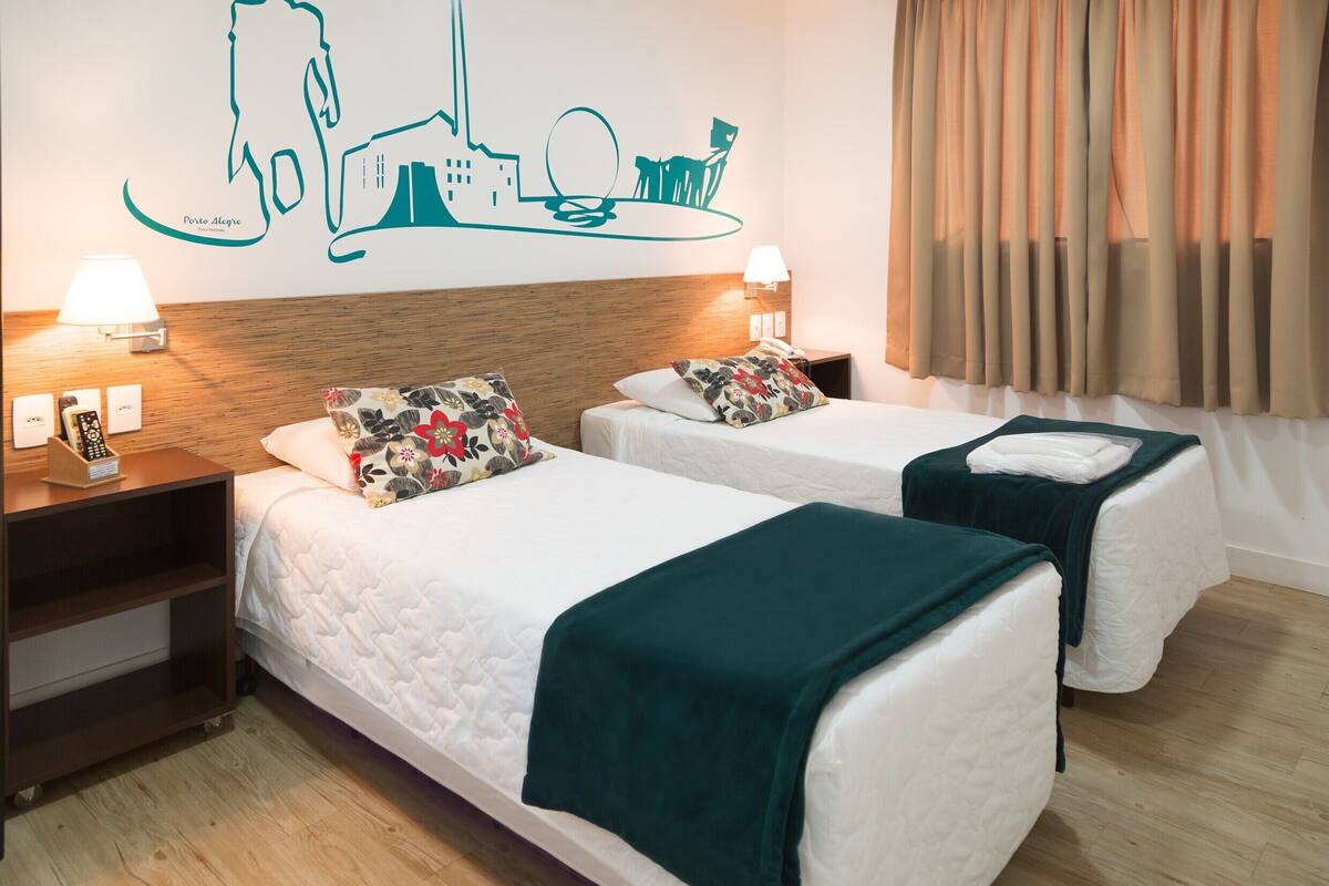 A hotel room with two beds, a wooden headboard, a wall mural, and a window with curtains.