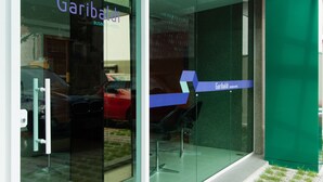 A modern building with a glass facade, a sign reading "Garibaldi Business Hotel," and a small outdoor area with grass and paving stones. - Garibaldi Business Hotel (Porto Alegre)
