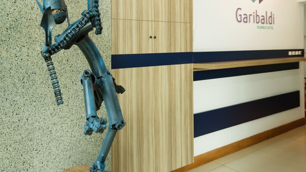 A sculpture on a wooden base in a hotel lobby with a sign reading "Garibaldi Business Hotel". - Garibaldi Business Hotel (Porto Alegre)