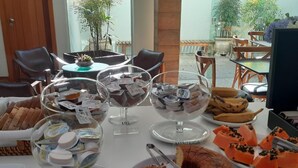 A buffet table with various food items including bread, cakes, and a variety of desserts in clear bowls. - Garibaldi Business Hotel (Porto Alegre)