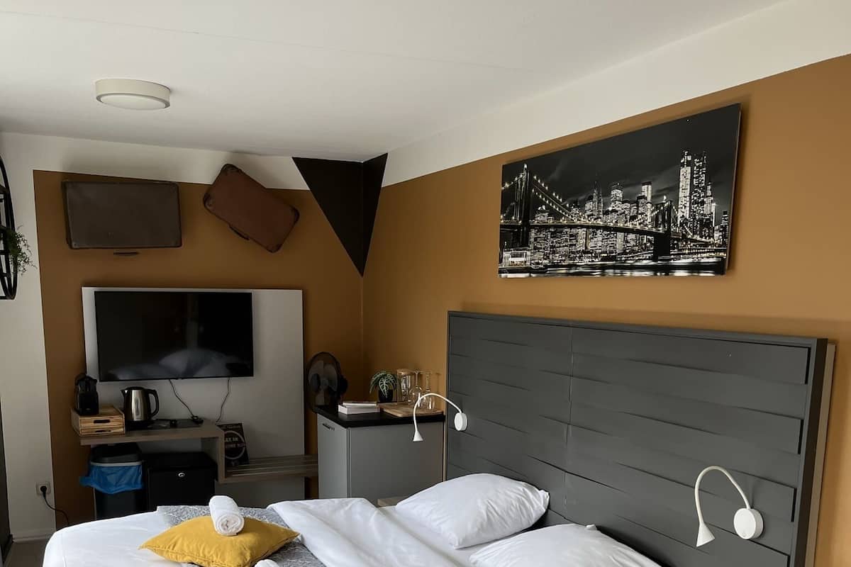 A modern hotel room with a large bed, a flat-screen TV, a desk, and a cityscape artwork on the wall.