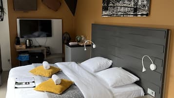 A modern hotel room with a large bed, a flat-screen TV, a desk, and a cityscape artwork on the wall.