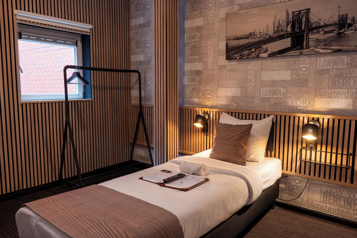 A hotel room with a bed, a window, a wall-mounted coat rack, and a cityscape painting.