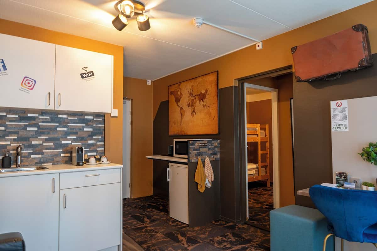 A compact kitchen with a microwave, coffee maker, and a small refrigerator. There is a bunk bed visible in the background, suggesting a shared sleeping area.
