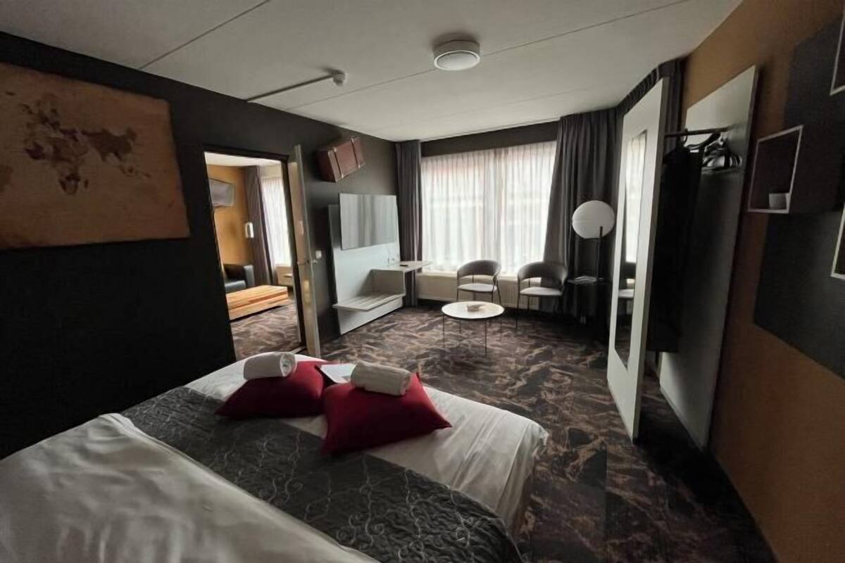 A hotel room with a bed, a desk, a chair, a TV, and a view of the outside.