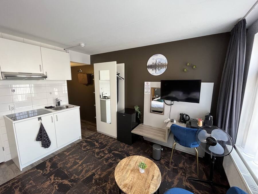 Habitación de hotel compacta con kitchenette, zona de comedor, televisor y ventana con cortinas.